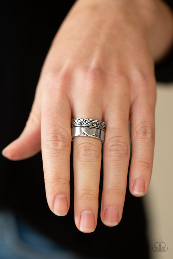 Bordered in a leafy embossed trim, a thick silver band is embossed in a heart for a vintage inspired look. Features a stretchy band for a flexible fit.  Sold as one individual ring.