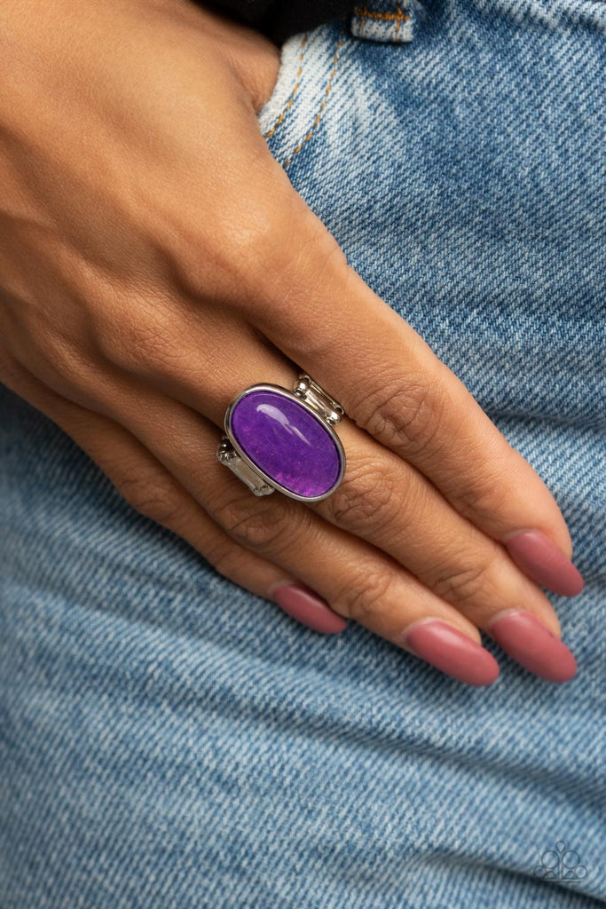 mystical-mantra-purple  An oval purple stone is encased inside a sleek silver frame, creating a mystical centerpiece atop the finger. Features a stretchy band for a flexible fit.  Sold as one individual ring.
