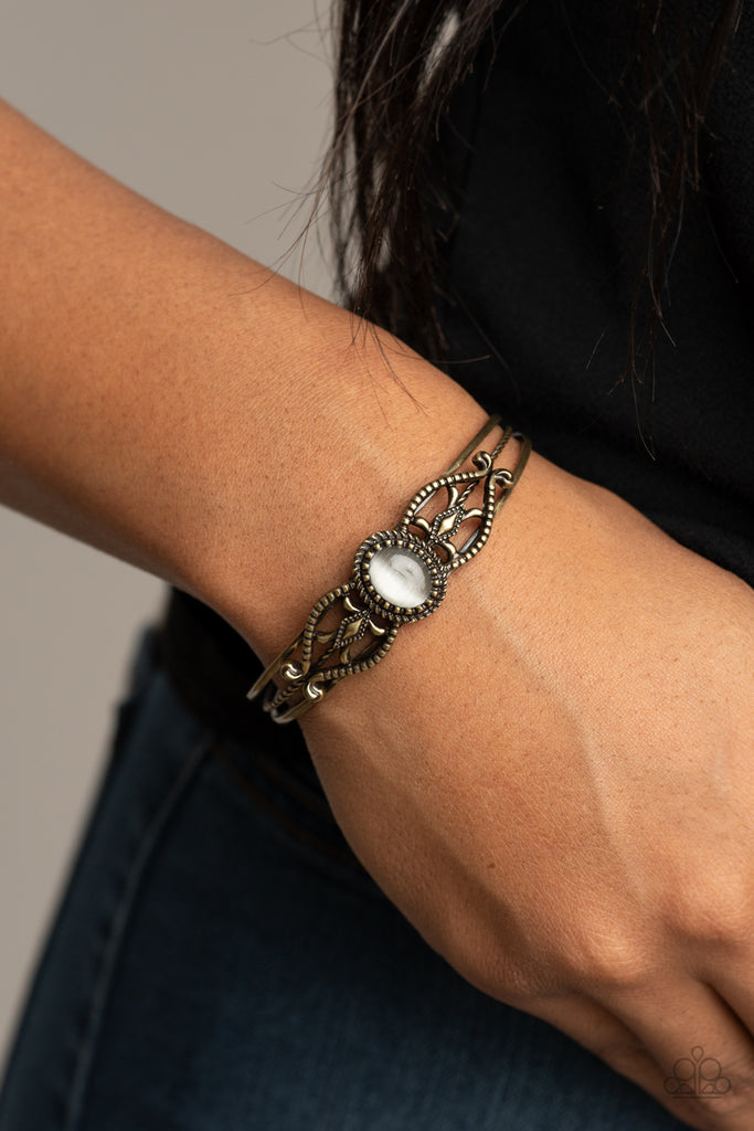 A frame of textured brass filigree whirls around an icy white cat's eye stone, creating a decorative centerpiece atop an ornately layered copper cuff.  Sold as one individual bracelet.  