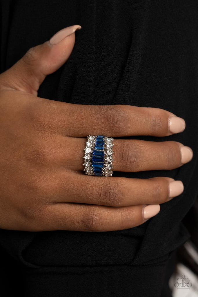Flanked between two sparkly rows of stunning white rhinestones, a row of glittery blue emerald cut rhinestones gradually increase in size at the center for a dramatically stacked look across the finger. Features a stretchy band for a flexible fit.  Sold as one individual ring.  