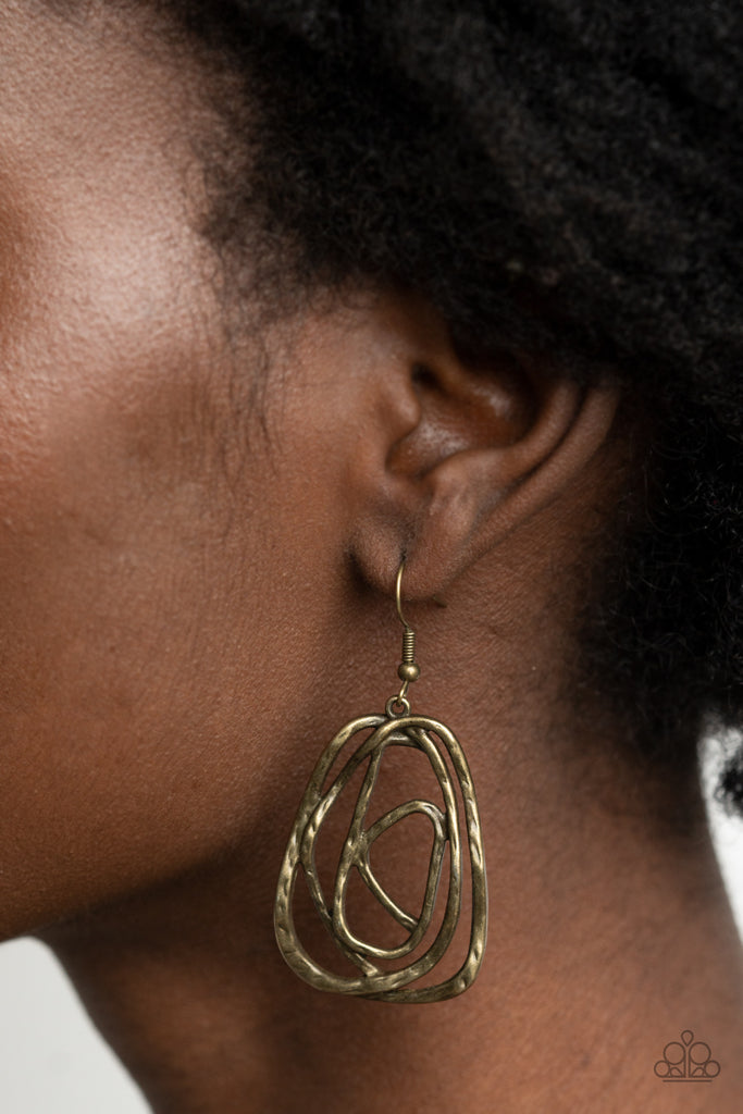 Featuring a hammered finish, a rustic brass wire delicately wraps into an asymmetrical frame for a dizzying artisan inspired look. Earring attaches to a standard fishhook fitting.  Sold as one pair of earrings.