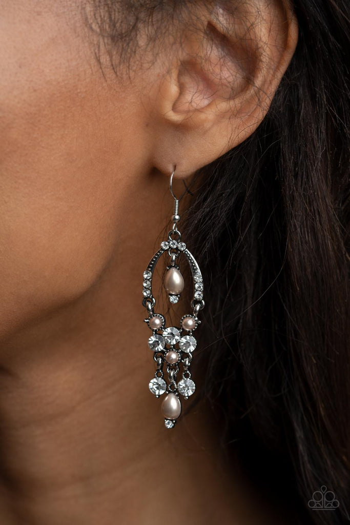 Glittery white rhinestones and pearly brown beaded fittings delicately swing from the bottom of an ornately embellished oval frame. A matching pearly frame dangles from the top of the decorative silver frame, adding timeless movement to the sparkly display. Earring attaches to a standard fishhook fitting.  Sold as one pair of earrings.