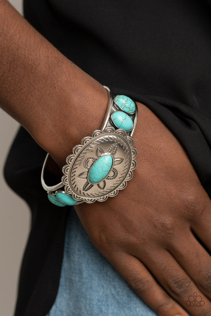 Dotted with a refreshing turquoise stone, a floral stamped scalloped silver frame sits atop a turquoise studded silver cuff, creating a southwestern inspired buckle atop the wrist.  Sold as one individual bracelet.