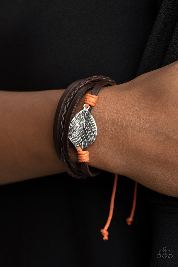 A lifelike silver leaf frame is knotted in place with orange cording across the front of a dainty brown leather band. Matching plain and braided leather bands join the centerpiece, creating earthy layers around the wrist. Features an adjustable sliding knot closure.  Sold as one individual bracelet.  