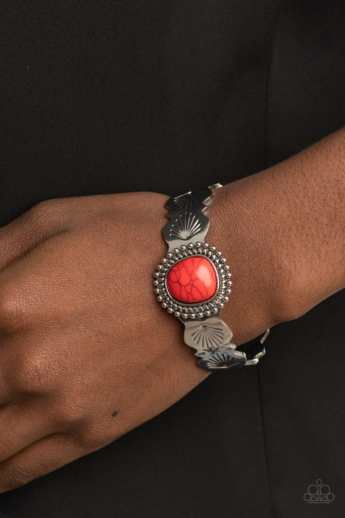 An asymmetrical red stone is pressed into the center of an abstract studded silver frame. The fiery stone piece sits off-center atop a scalloped silver cuff stamped in seashell patterns, creating a whimsical centerpiece around the wrist.  Sold as one individual bracelet.  