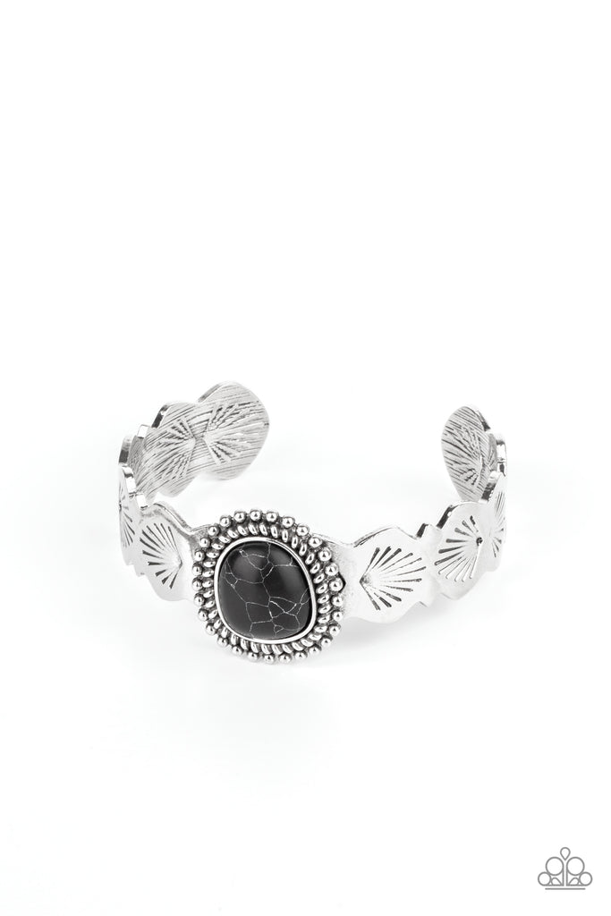 An asymmetrical black stone is pressed into the center of an abstract studded silver frame. The earthy stone piece sits off-center atop a scalloped silver cuff stamped in seashell patterns, creating a whimsical centerpiece around the wrist.  Sold as one individual bracelet.