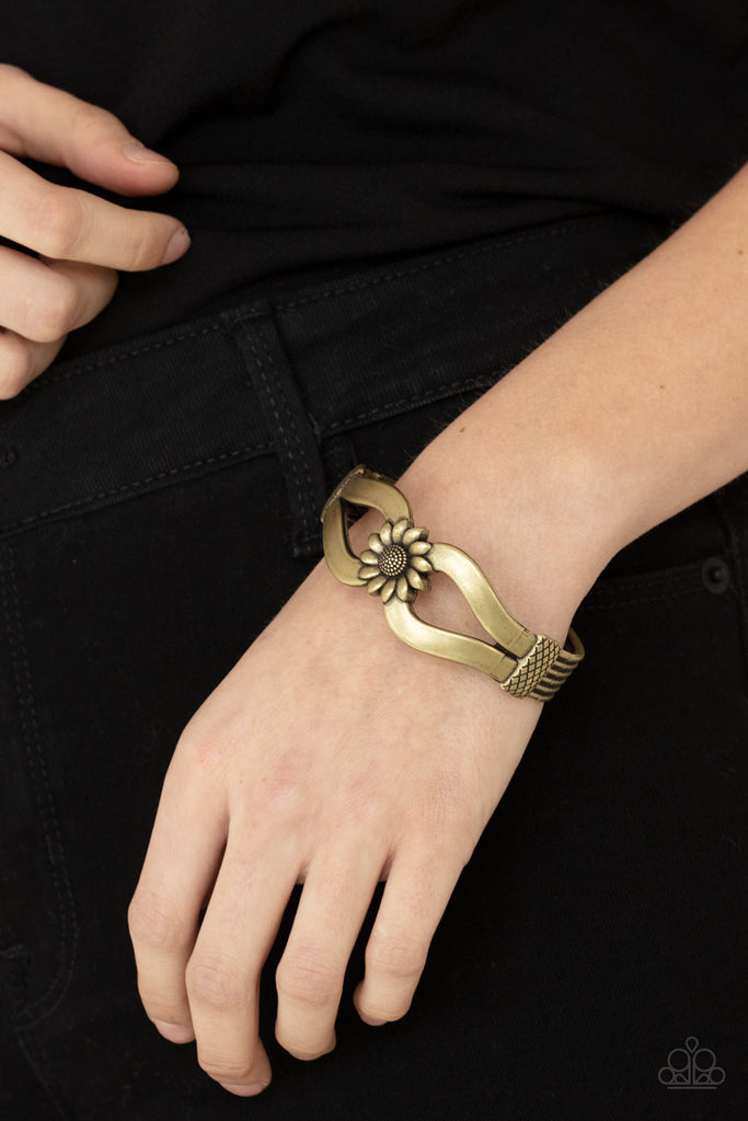 let-a-hundred-sunflowers-bloom-brass  Antiqued brass ribbons loop out from a decorative brass sunflower that attaches to a ribbed brass frame, creating a cuff-like bangle around the wrist. Features a hinged closure.  Sold as one individual bracelet.