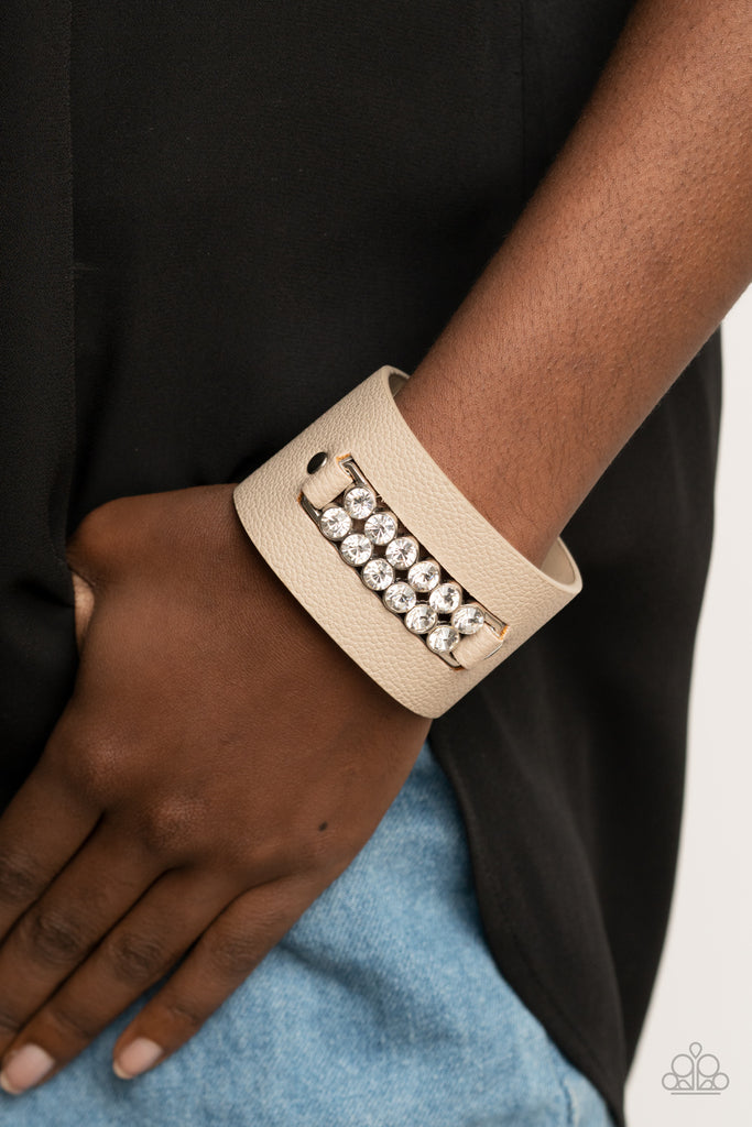 Two rows of oversized white rhinestones are studded in place across the center of a thick leather band, creating a sassy centerpiece around the wrist. Features an adjustable snap closure.  Sold as one individual bracelet.