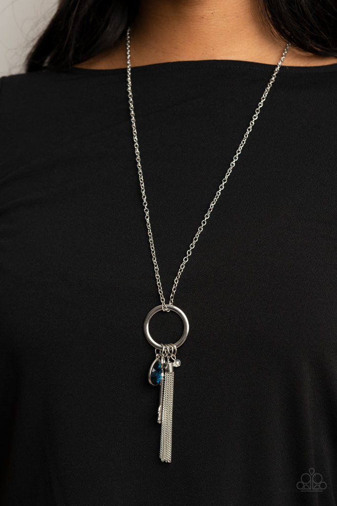 A blue teardrop gem, silver key, dainty crystal-like bead, and shimmery silver chain tassel swings from the bottom of a silver ring at the bottom of a lengthened silver chain, creating a whimsically tasseled display. Features an adjustable clasp closure.  Sold as one individual necklace. Includes one pair of matching earrings.
