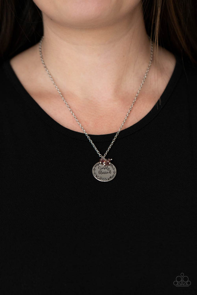 Bordered in a leafy pattern, a shiny silver disc is stamped with the phrase, "Simply Blessed," joins a dainty cluster of iridescent purple crystal-like beads at the bottom of a chain, creating an inspirational pendant below the collar. Features an adjustable clasp closure.  Sold as one individual necklace. Includes one pair of matching earrings.