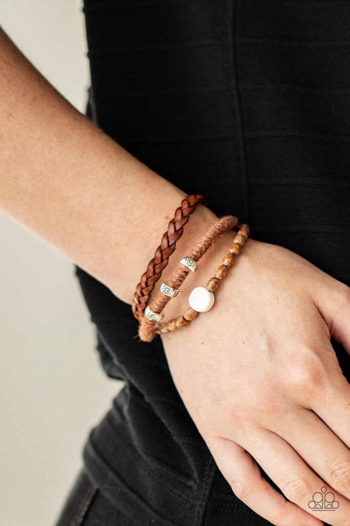 Featuring floral stamped accents and a white ceramic-like bead, strands of wooden beads, brown twine, and braided leather layer around the wrist for an earthy look. Features an adjustable sliding knot closure.  Sold as one individual bracelet.  New Kit
