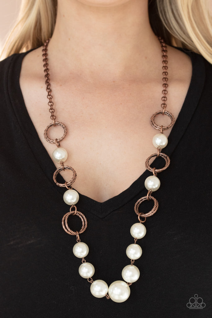 A dramatic collection of oversized white pearls and textured copper rings interconnect across the chest, creating a bold display of refinement. Features an adjustable clasp closure.  Sold as one individual necklace. Includes one pair of matching earrings.  
