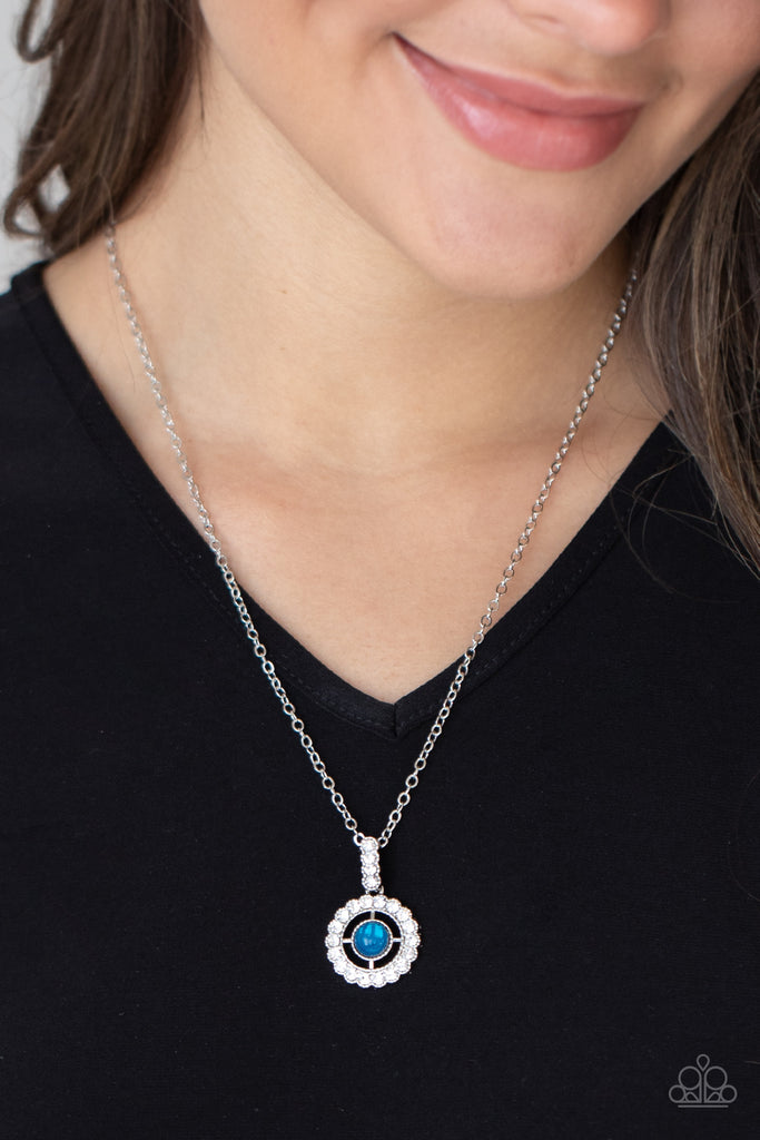A white rhinestone encrusted fitting attaches to a ring of white rhinestones dotted with a glassy Blue Tint beaded center, creating a twinkly pendant at the bottom of a classic silver chain. Features an adjustable clasp closure.  Sold as one individual necklace. Includes one pair of matching earrings.  