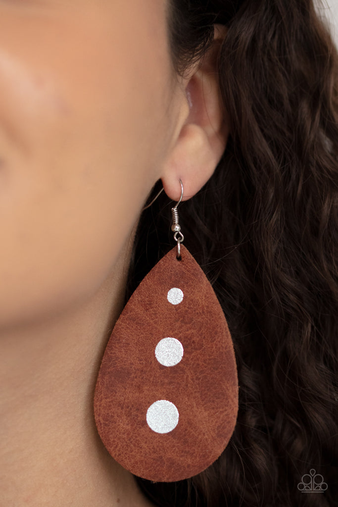 The front of a distressed leather teardrop frame is adorned into three shimmery silver paint drops, creating a rustic elegance. Earring attaches to a standard fishhook fitting.  Sold as one pair of earrings.