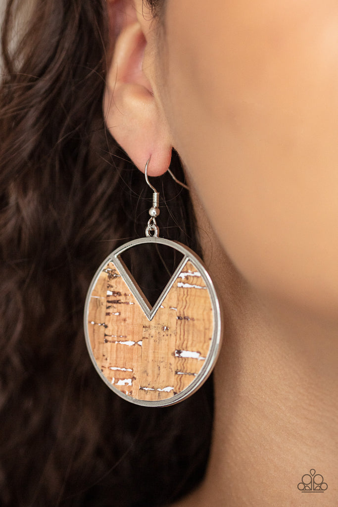 Featuring hints of white accents, an earthy piece of cork is placed into the center of a circular hoop. A triangular slice is removed from the cork, creating an edgy airy finish. Earring attaches to a standard fishhook fitting.  Sold as one pair of earrings.