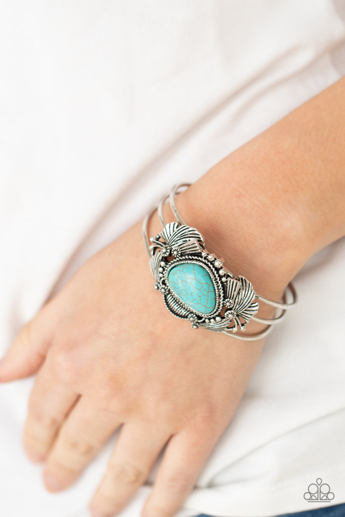 An asymmetrical turquoise stone is pressed into the center of a rustic silver centerpiece stacked with flared silver frames, shiny studs, and antiqued floral accents. The whimsical frames sit atop a layered cuff, creating a seasonal display around the wrist.  Sold as one individual bracelet.  New Kit