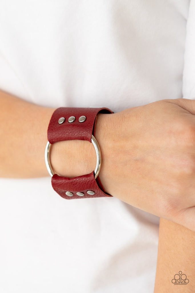 An oversized silver hoop is studded in place between the center of studded pieces of red and black leather, creating a rustic centerpiece around the wrist. Features an adjustable snap closure.  Sold as one individual bracelet.  