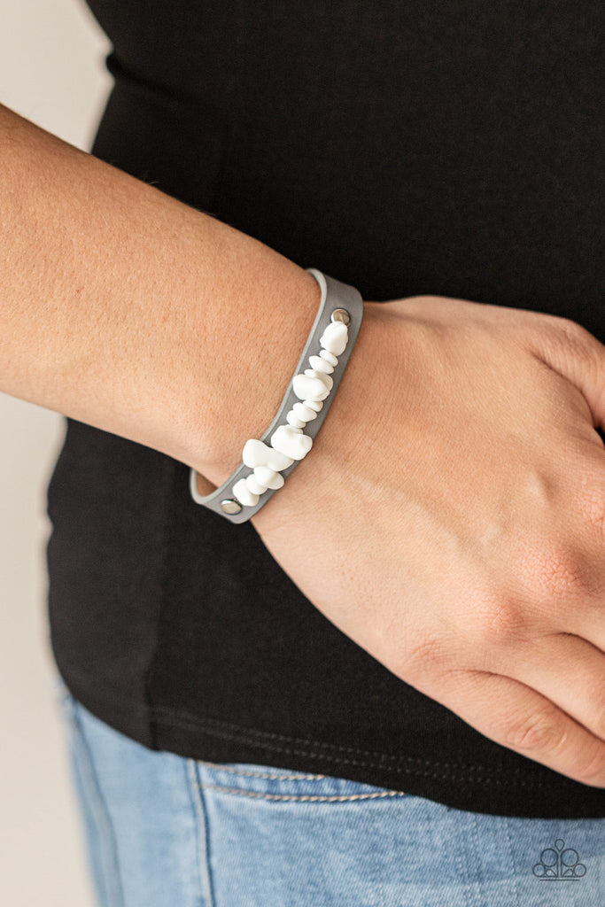 A strand of white pebbles is studded in place across the front of a skinny gray leather band, creating a colorful earthy display around the wrist. Features an adjustable snap closure.  Sold as one individual bracelet.