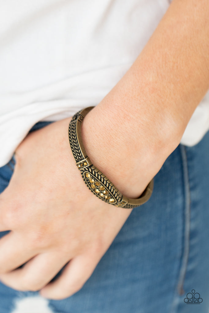 Featuring an aurum rhinestone encrusted centerpiece, a rustic brass cuff-like bangle is embossed in antiqued rope-like texture for a gritty-glamorous look. Features a hinged closure.  Sold as one individual bracelet.