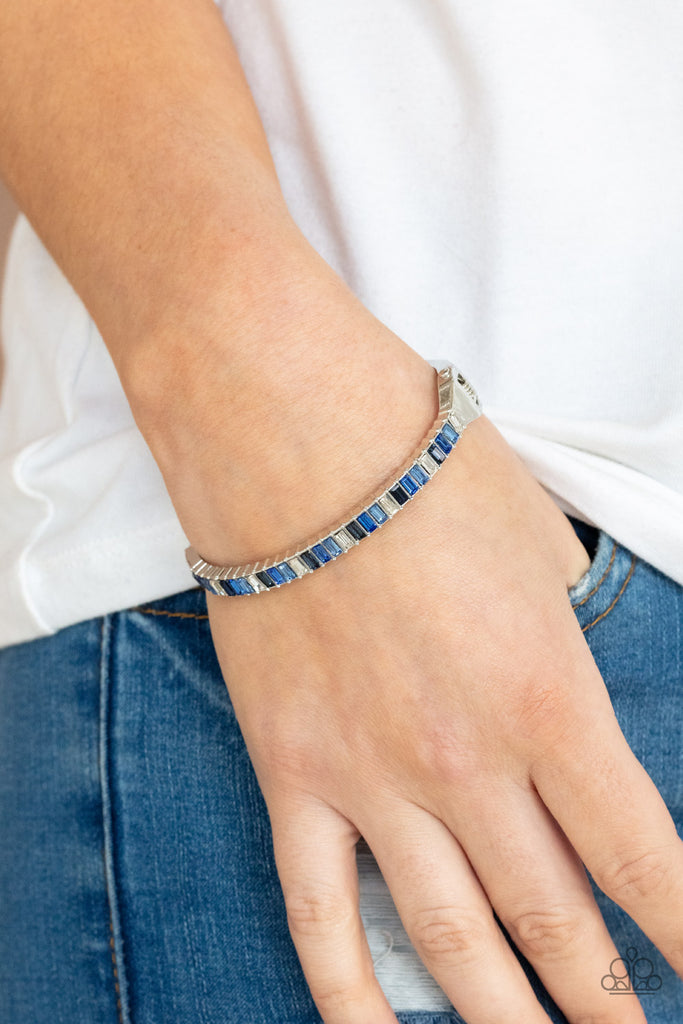 toast-to-twinkle-blue  Featuring regal emerald style cuts, a dainty row of blue and white rhinestones are encrusted across the front of a silver cuff-like bangle for a timeless fashion. Features a hinged closure.  Sold as one individual bracelet.