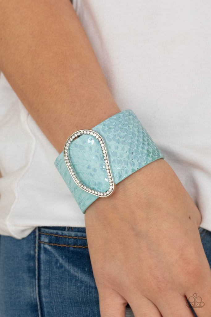 Encrusted with glassy white rhinestones, an asymmetrical silver fitting glides along a blue leather band adorned in a metallic python print for a wild look. Features an adjustable snap closure.  Sold as one individual bracelet.  