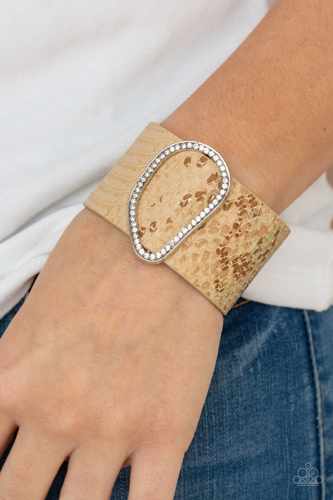 Encrusted with glassy white rhinestones, an asymmetrical silver fitting glides along a tan leather band adorned in a golden metallic python print for a wild look. Features an adjustable snap closure.  Sold as one individual bracelet.