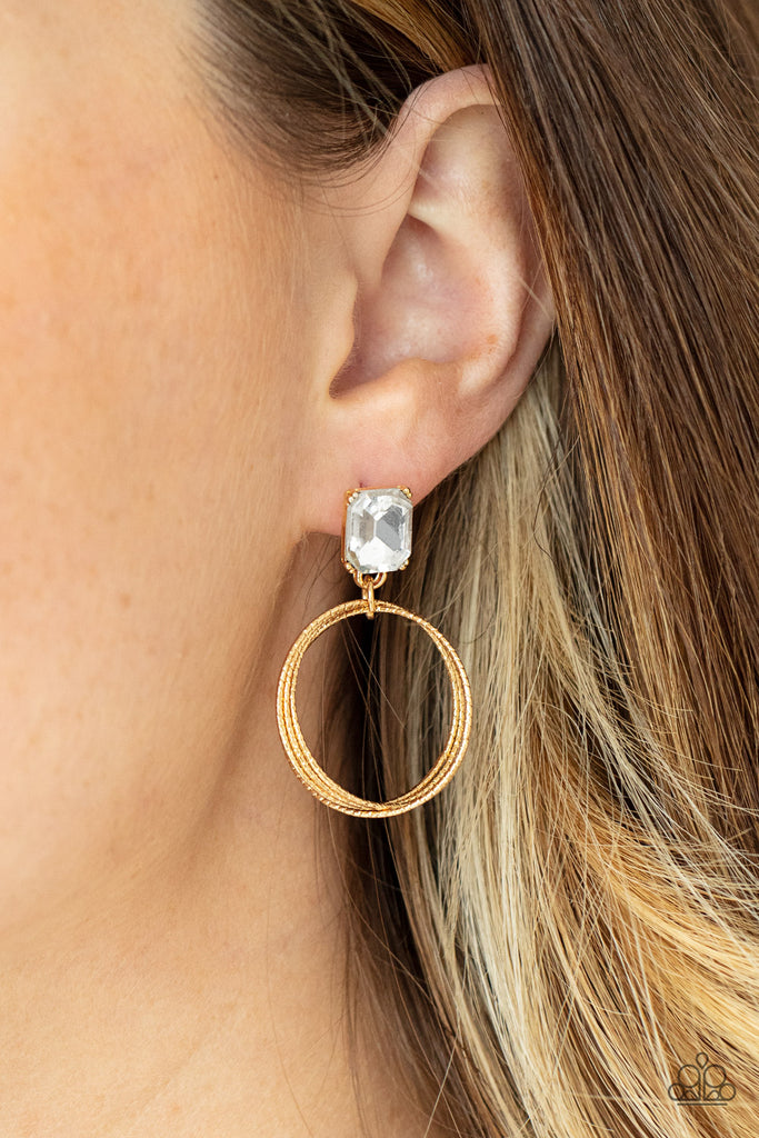 Encased in a pronged gold setting, a white emerald cut rhinestone links with a trio of refined textured gold rings, creating a romantic lure. Earring attaches to a standard post fitting.  Sold as one pair of post earrings.