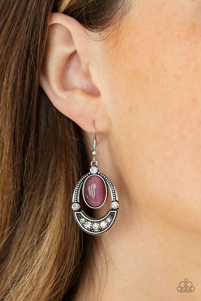 A glowing purple cat's eye stone attaches to the top of a studded silver frame. The bottom of the oval is encrusted in glassy white rhinestones, creating a whimsical display. Earring attaches to a standard fishhook fitting.  Sold as one pair of earrings.