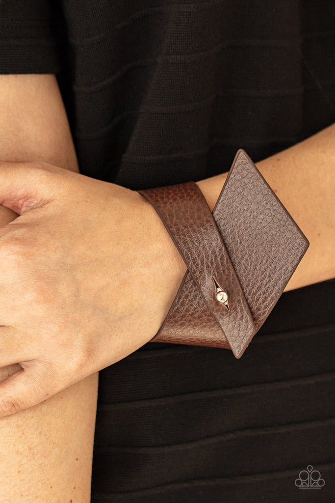 A triangular piece of brown leather delicately wraps around the wrist, creating an edgy asymmetrical centerpiece around the wrist. Features a studded button loop closure.  Sold as one individual bracelet.