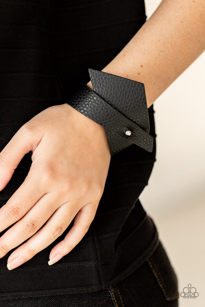 A triangular piece of black leather delicately wraps around the wrist, creating an edgy asymmetrical centerpiece around the wrist. Features a studded button loop closure.  Sold as one individual bracelet.  