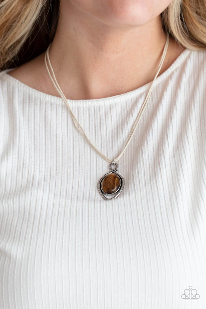 An oversized tiger's eye stone is pressed into a silver oval frame and outlined with an unexpected irregular shaped frame. The eye-catching pendant suspends from a double strand of white cord below the collar for a mysterious finish. Features an adjustable clasp closure.  Sold as one individual necklace.