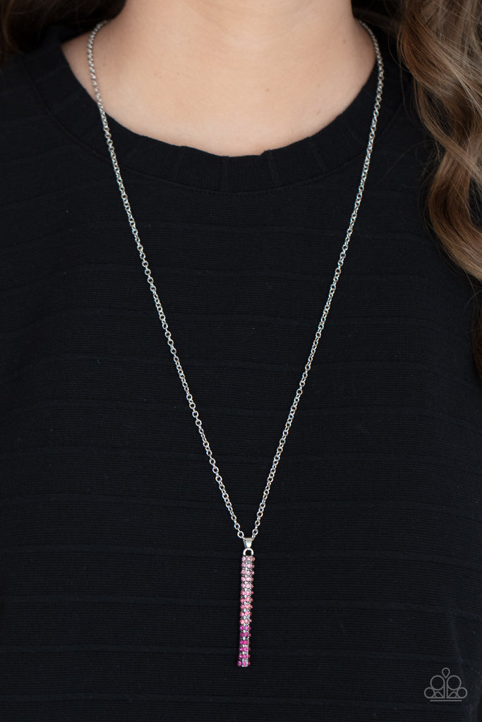 A sparkly collection of spectrum pink rhinestones are encrusted along a silver pendulum that swings along the bottom of a silver chain, creating a glittery ombre effect. Features an adjustable clasp closure.  Sold as one individual necklace. Includes one pair of matching earrings.
