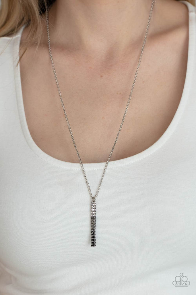 A sparkly collection of white, smoky, and black rhinestones are encrusted along a silver pendulum that swings along the bottom of a silver chain, creating a glittery ombre effect. Features an adjustable clasp closure.  Sold as one individual necklace. Includes one pair of matching earrings.