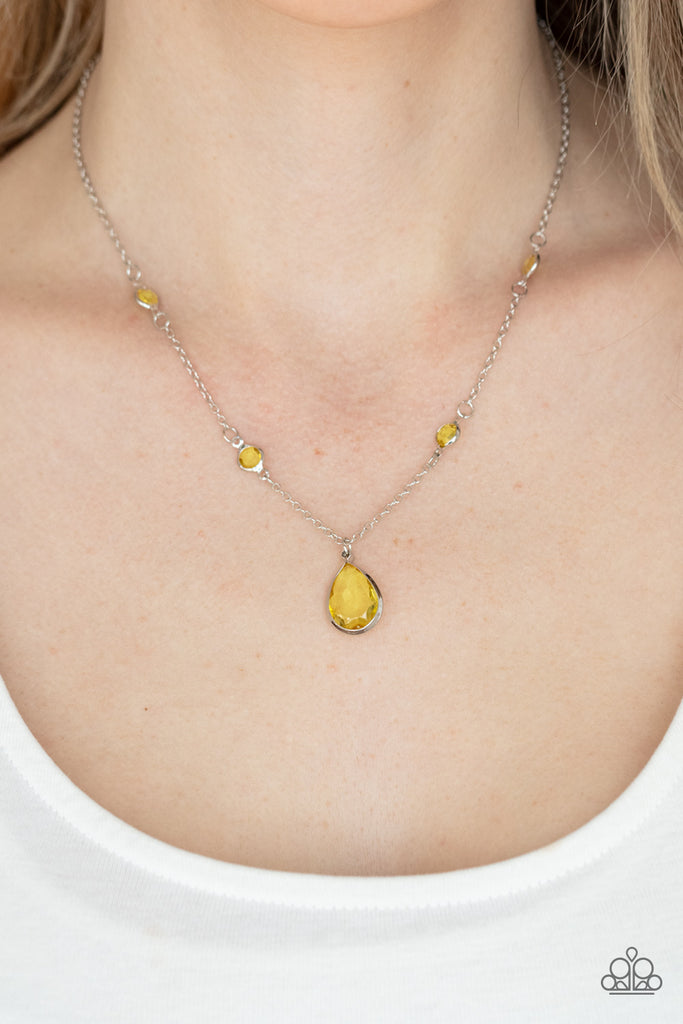A glassy yellow teardrop gem encased in a silver frame dips elegantly below the collar. Small round yellow gems accent the silver chain for a delicate and dreamy display. Features an adjustable clasp closure.  Sold as one individual necklace. Includes one pair of matching earrings.