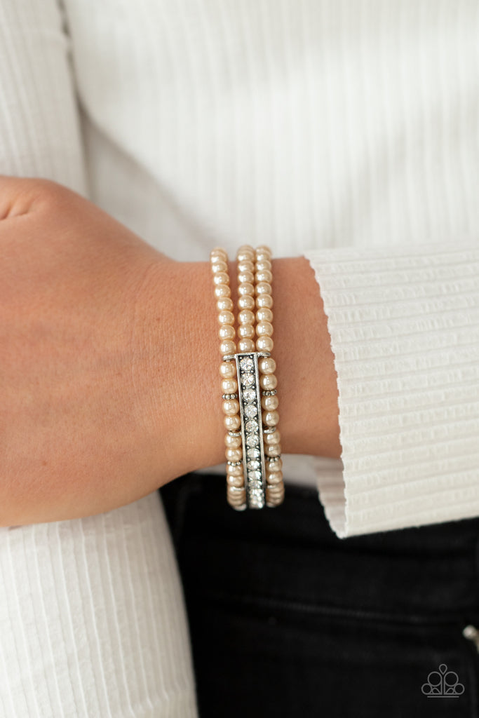 Threaded along stretchy bands, three rows of dainty brown pearls are held in place around the wrist by a white rhinestone encrusted centerpiece for a romantic flair.  Sold as one individual bracelet.