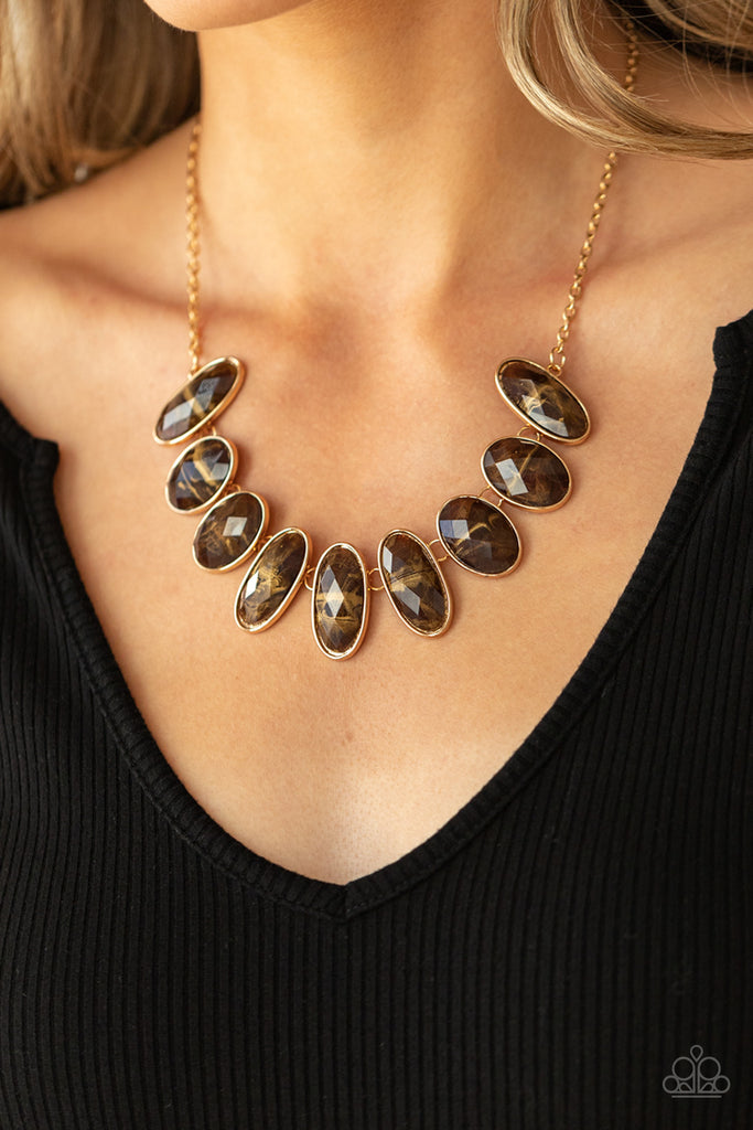 Generous glossy brown gems, dusted in shimmery gold, lay in oval gold frames and link across the collar creating a glimmering statement. Features an adjustable clasp closure.  Sold as one individual necklace. Includes one pair of matching earrings.