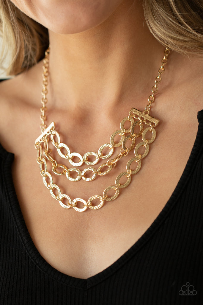 Three rows of gold chains with oversized hammered oval links attach to gold bars for an edgy display below the collar. Features an adjustable clasp closure.  Sold as one individual necklace. Includes one pair of matching earrings.