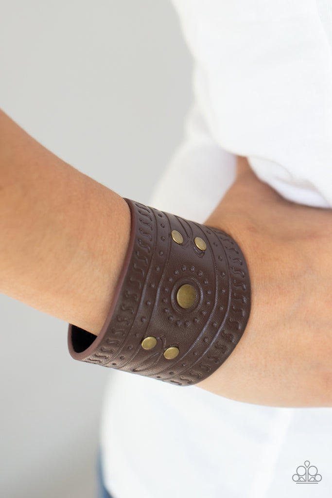 Dotted in rustic brass studs, a triangular piece of brown leather is stamped in indigenous inspired patterns for an urban flair. Features an adjustable snap closure.  Sold as one individual bracelet.