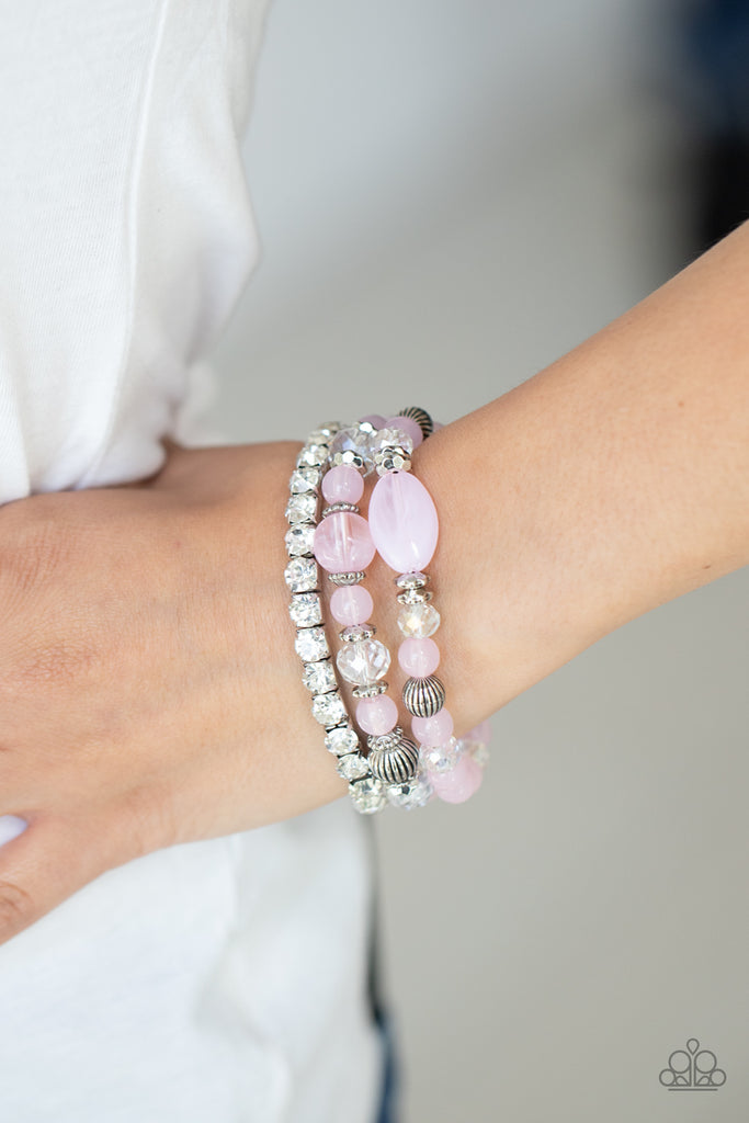 Infused with a stretchy strand of glassy white rhinestones, a mismatched collection of cloudy pink, white crystal-like, and ornate silver accents are threaded along stretchy bands around the wrist, creating ethereal layers.  Sold as one set of three bracelets.