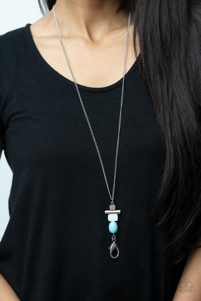 A square wooden frame, silver rod, piece of white shell, and oval turquoise stone stack into a seasonal pendant at the bottom of a lengthened silver chain. A lobster clasp hangs from the bottom of the design to allow a name badge or other item to be attached. Features an adjustable clasp closure.  Sold as one individual lanyard. Includes one pair of matching earrings.  New Kit