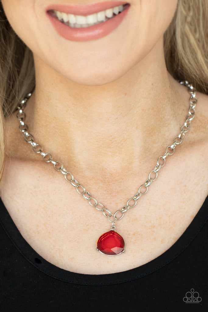 An oversized glassy red gem is pressed into a pronged silver fitting at the bottom of a chunky silver chain, creating a dramatic pendant below the collar. Features an adjustable clasp closure.  Sold as one individual necklace. Includes one pair of matching earrings.  