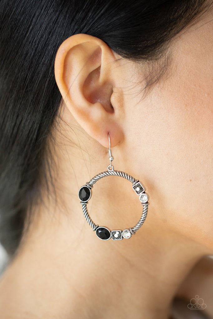 A glittery collection of black oval, square hematite, and classic white rhinestones haphazardly adorn the front of a textured silver hoop, for a gritty-glamorous look. Earring attaches to standard fishhook fittings.  Sold as one pair of earrings.