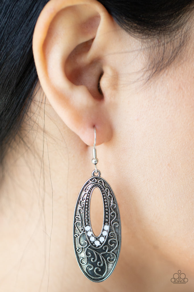 Dainty silver studs fade into dewy white rhinestones around the airy center of an oval silver frame that is embossed in vine-like scroll, creating an ethereally whimsical frame. Earring attaches to a standard fishhook fitting.  Sold as one pair of earrings.