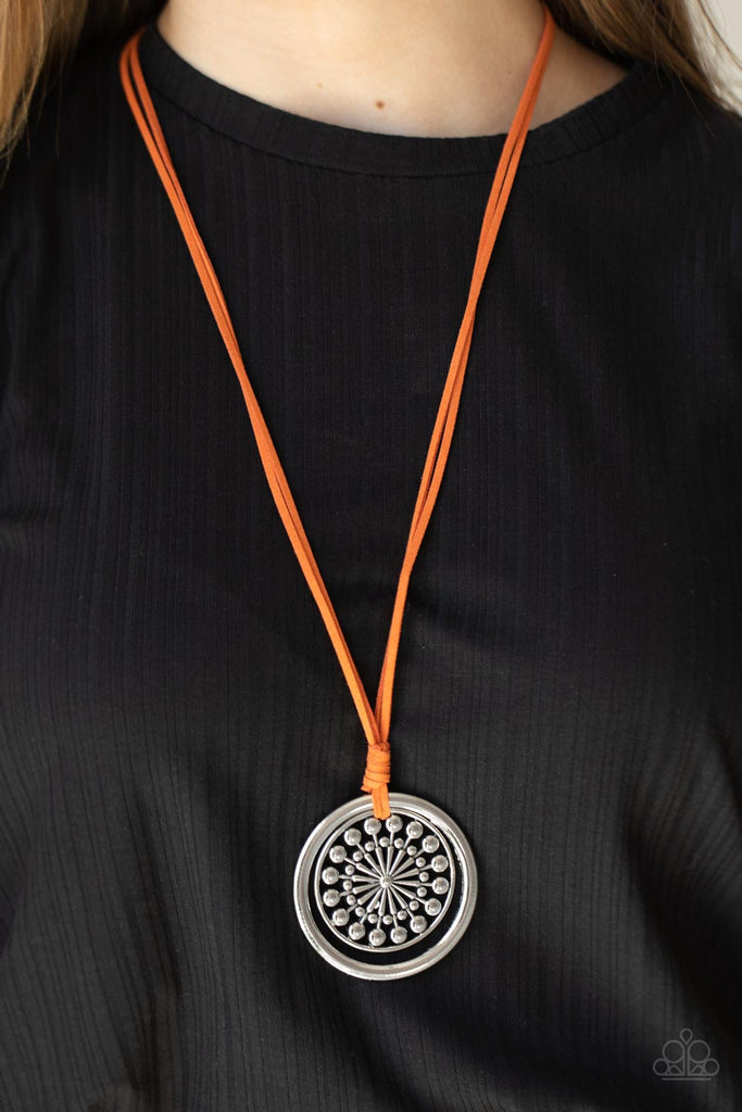 A lengthened piece of orange suede cording is knotted around a silver ring and decorative studded silver frame, creating a whimsy mandala-like pendant. Features an adjustable clasp closure.  Sold as one individual necklace. Includes one pair of matching earrings.