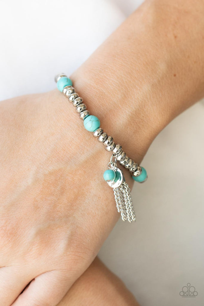 An earthy collection of hammered silver beads and round turquoise stones are threaded along a stretchy band around the wrist. A dainty silver tassel, hammered silver disc, and a turquoise stone swing from the seasonal display, adding playful movement to the whimsy look.  Sold as one individual bracelet.