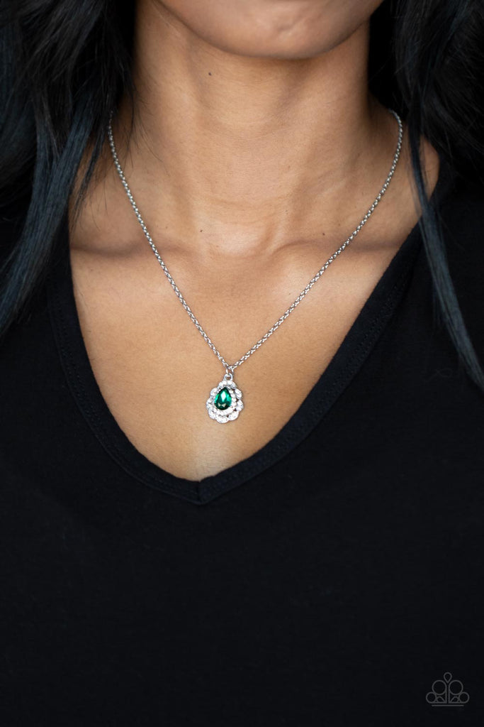 A glittery green teardrop gem is pressed into the center of a pronged border of glassy white rhinestones that sits atop a ring of a silver frame dotted in pairs of white rhinestones. The glittery pendant swings from the bottom dainty silver chain, creating a vintage inspired pendant below the collar. Features an adjustable clasp closure.  Sold as one individual necklace. Includes one pair of matching earrings.