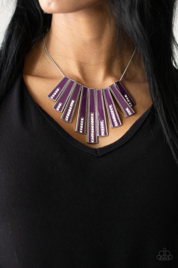 fan-tastically-deco-purple Encased in daintily dotted silver frames, a row of flared silver bars painted in a glossy purple, fans out across the collar. A column of sparkling white rhinestones rises from the bottom of each frame, creating a dramatically deco finish as they sway from a round silver chain. Features an adjustable clasp closure.  Sold as one individual necklace. Includes one pair of matching earrings.
