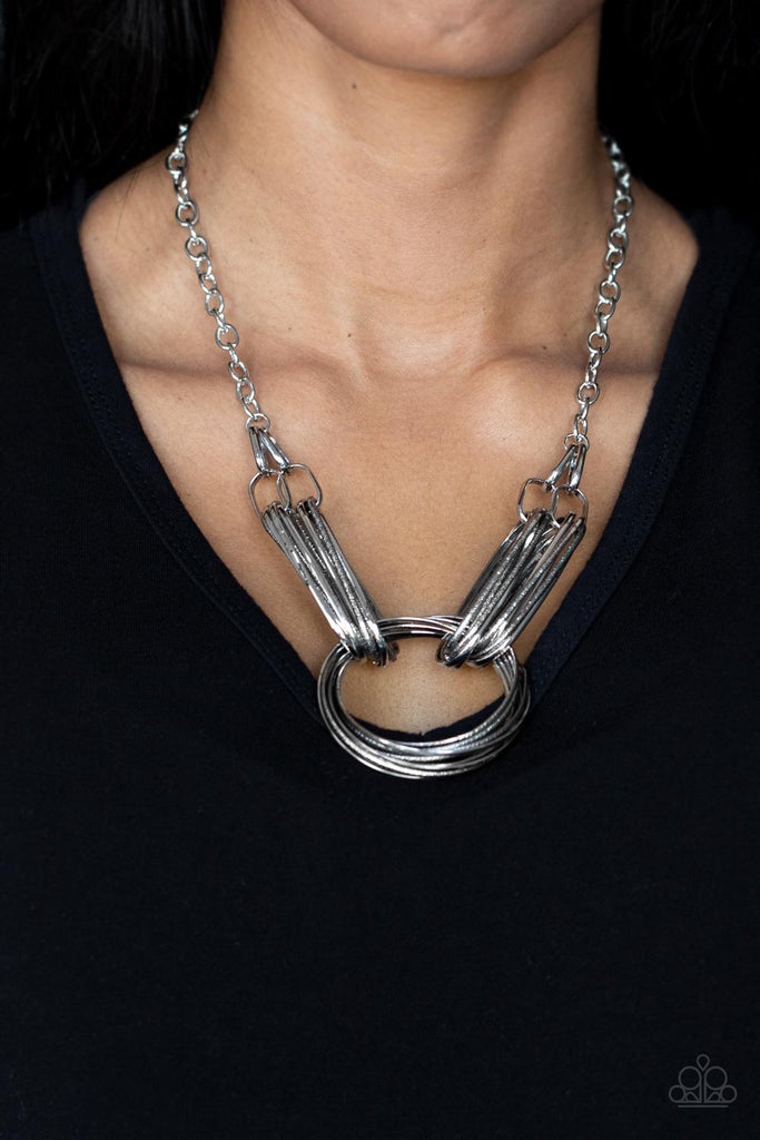 lip-sync-links-silver Layers of oblong silver links connect to a collection of oversized textured and shiny silver rings creating a dramatic centerpiece. Attached to a silver chain, the rustic links create an unconventionally edgy statement below the collar. Features an adjustable clasp closure.  Sold as one individual necklace. Includes one pair of matching earrings.