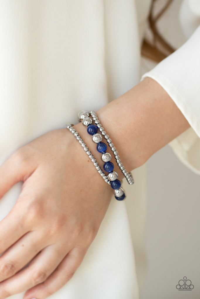 Infused with two strands of dainty silver beads, a collection of glassy blue cat's eye beads and shiny silver beads are threaded along stretchy bands around the wrist for a whimsically layered look.  Sold as one set of three bracelets.