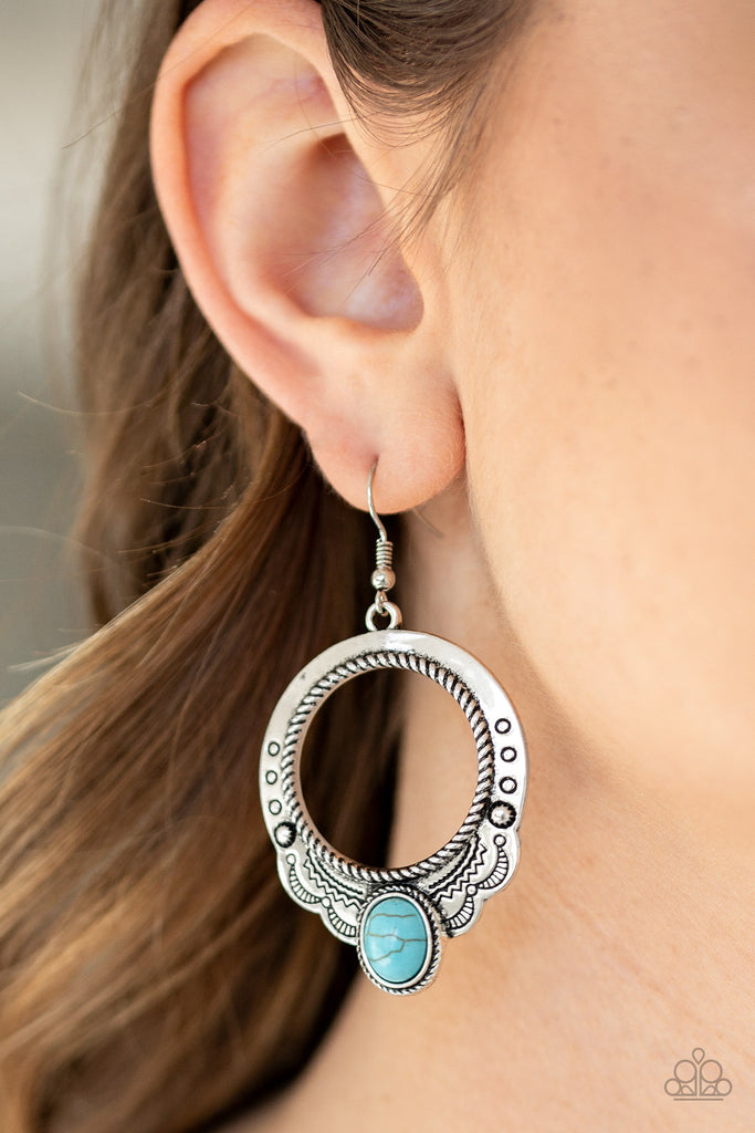 An oval turquoise stone is pressed into the bottom of a scalloped silver hoop stamped and studded in trendy patterns for a southwestern inspired look. Earring attaches to a standard fishhook fitting.  Sold as one pair of earrings.